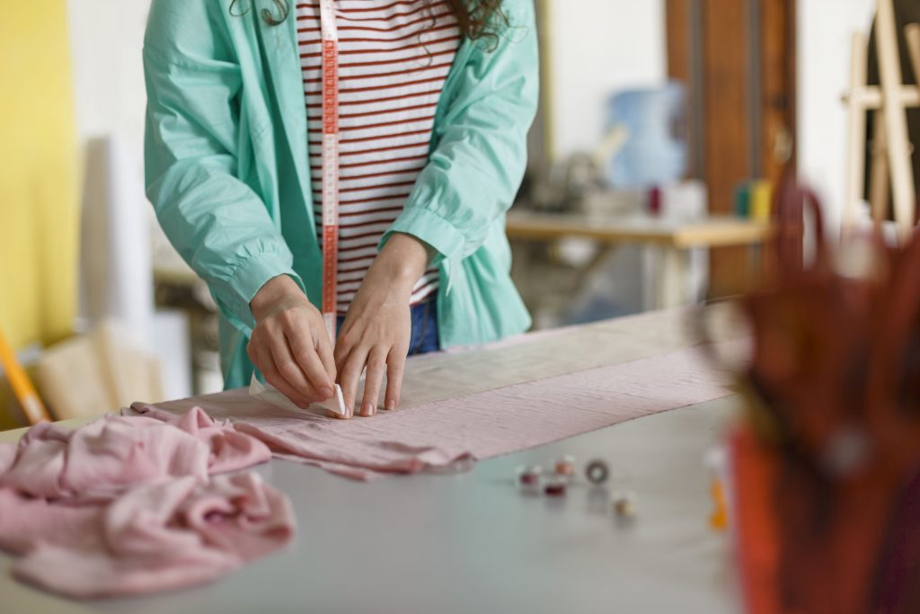 close up seamstress drawing with soap on pink textile in sewing